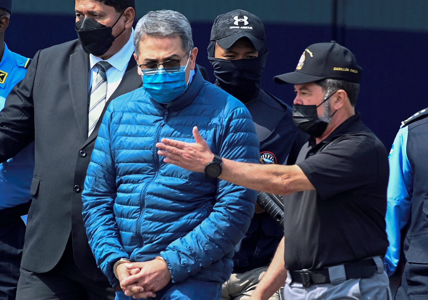 Honduras' former President Juan Orlando Hernandez (C) is escorted by Minister of Security Ramon Sabillon (R) towards a plane of the US Drug Enforcement Agency (DEA), during his extraditaton to United States at the Air force Base, in Tegucigalpa, on April 21, 2022. (Photo by Orlando SIERRA / AFP)