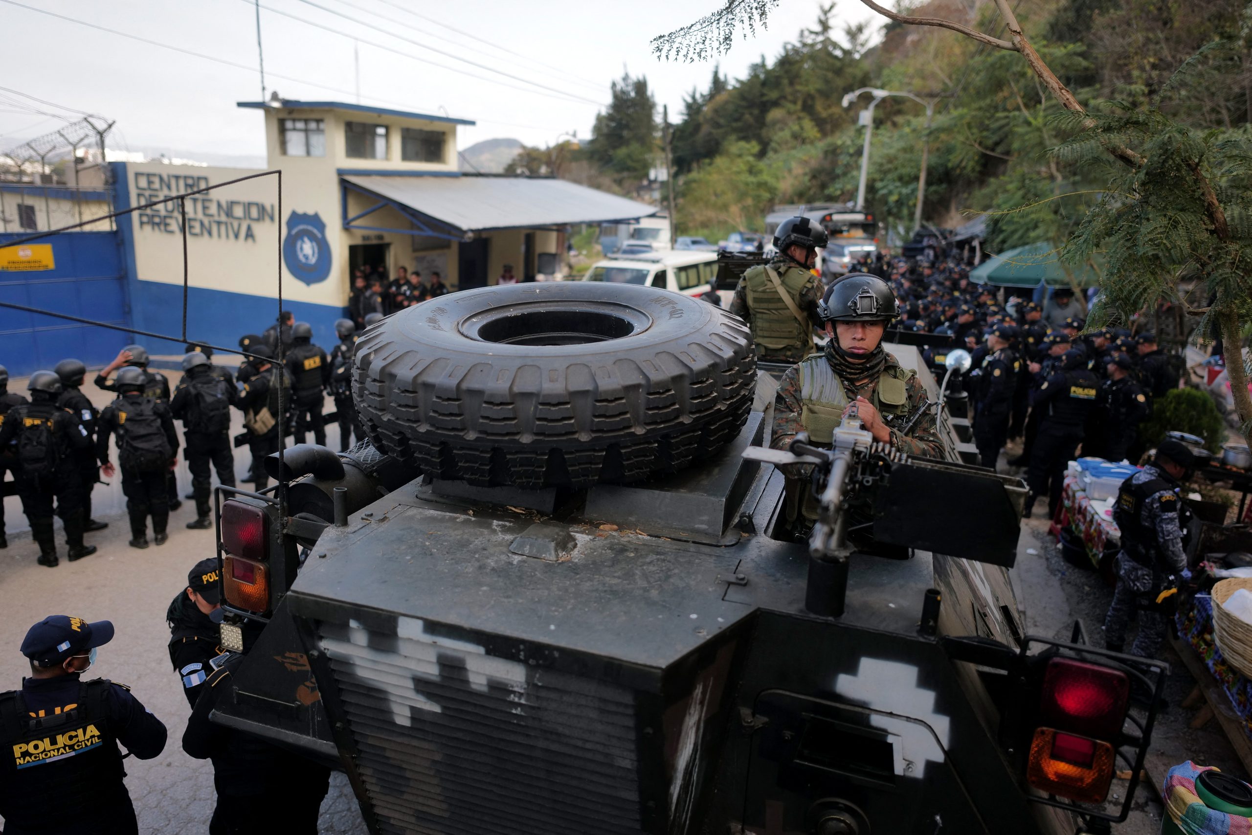 A Guatemalan soldier in an armored vehicle and members of the Police Special Forces Division (FEP) guard the entrance to the men's Preventive Detention Center in Guatemala City on January 18, 2026. Guatemala's government accused gang members of killing eight police officers in several attacks on January 18, 2025, after refusing to negotiate the transfer of leaders of these dangerous gangs to a lower-security prison. The killings occurred a day after gang-affiliated inmates took 46 people hostage in three prisons across the country. Police regained control of one of the prisons. (Photo by Edwin BERCIAN / AFP)