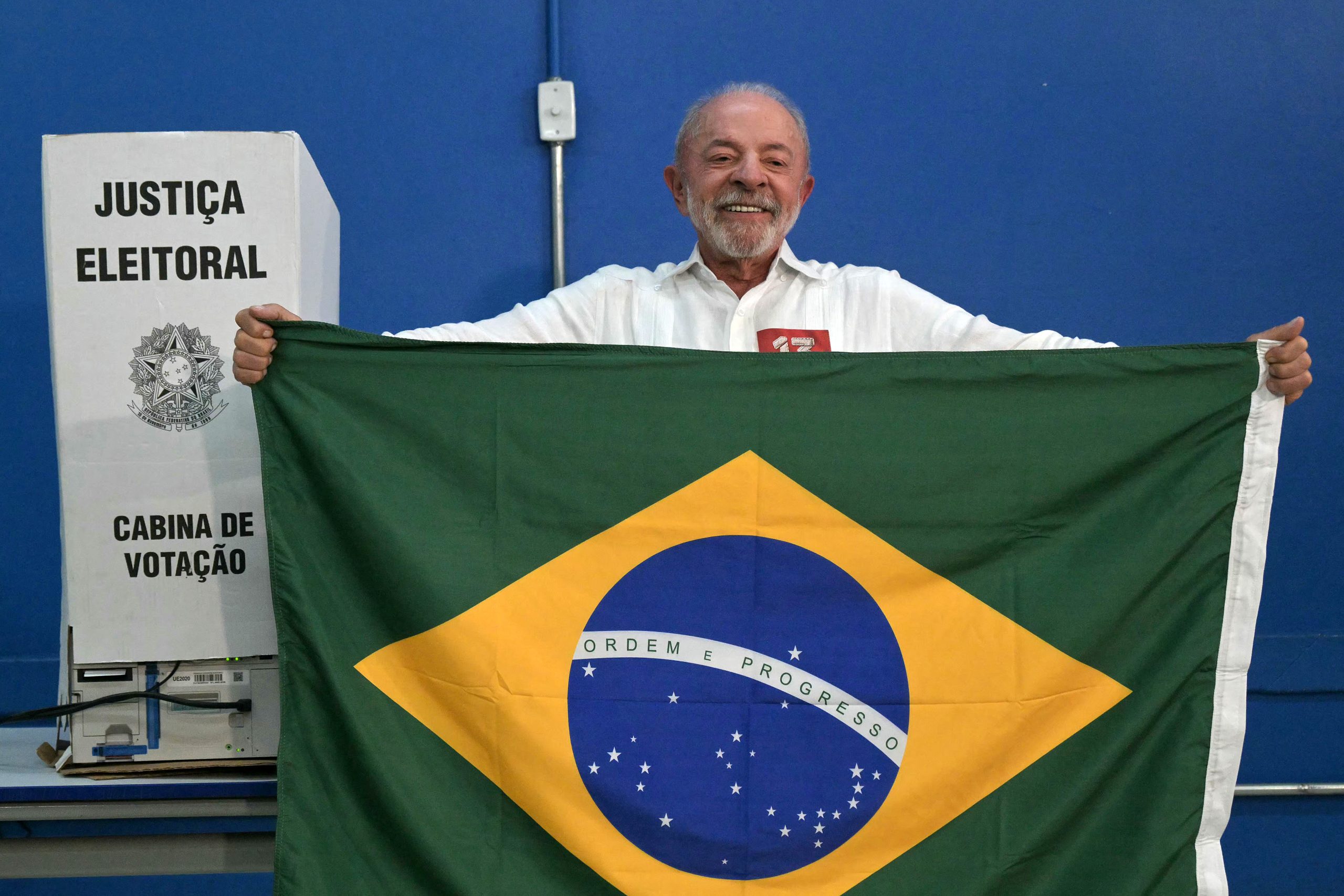 Brazil's President and Workers' Party (PT) re-election candidate Luiz Inacio Lula da Silva holds a Brazilian flag at a polling station during the presidential runoff election in Sao Bernardo do Campo, Sao Paulo state, Brazil, on October 25, 2026. Lula da Silva faces right-wing senator Flavio Bolsonaro in a runoff that will determine whether Brazil remains one of the few leftist nations in the region or joins a regional swing to the right championed by US President Donald Trump, Bolsonaro's ally. (Photo by NELSON ALMEIDA / AFP)